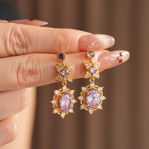 Macro detail of vintage gold earrings featuring purple zircon flower and bow design