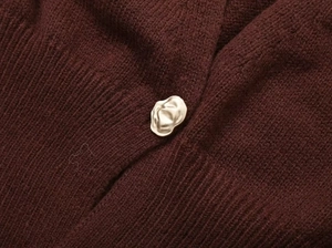 Close-up of burgundy knitted cardigan with a textured wavy gold metal button detail