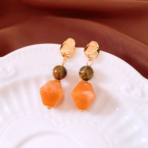 Detail of beaded irregular earrings with golden metal and tiger eye resin pendants