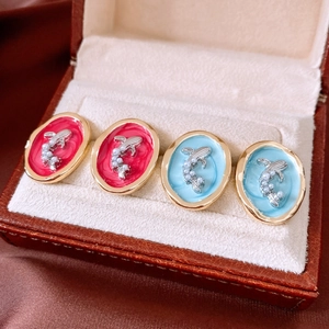 Detail view of oval enamel pearl earrings in red and sky blue on a premium jewelry box display
