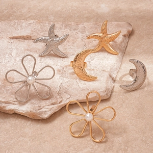 Gold and silver open rings with starfish moon and pearl flower charms on a stone