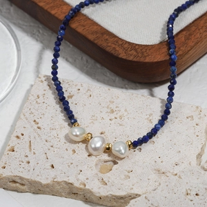 Blue lapis lazuli beaded necklace with baroque pearls on a textured stone surface