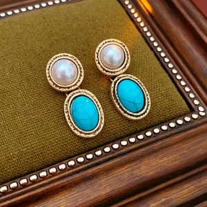 Detail of vintage gold earrings with pearls and turquoise stone on green fabric