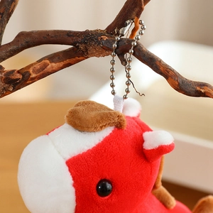 Close-up of red and white plush pony keychain hanging on a branch with silver ball chain
