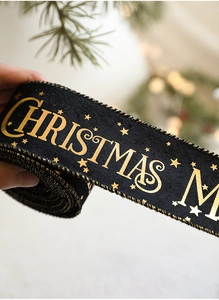 Detail of Christmas ribbon with gold foil stars and Merry Christmas lettering on black fabric