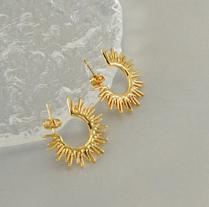 Macro detail of golden sunburst earrings with butterfly backs on textured glass
