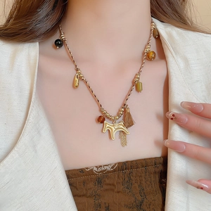 Close-up of woven necklace featuring gold horse pendant and metallic fringe tassels