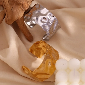 Close-up of gold and silver hammered metal bangles with textured ripples on soft fabric