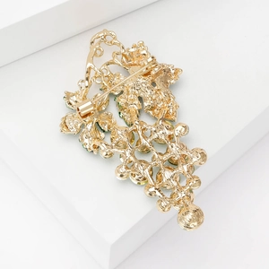 Back view of gold grape brooch with green accents on minimalist white geometric display