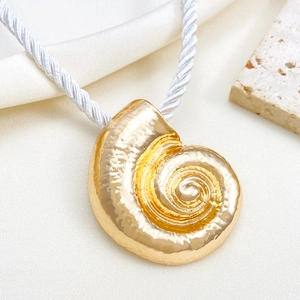 Golden shell pendant necklace with white woven cord on natural stone and soft fabric