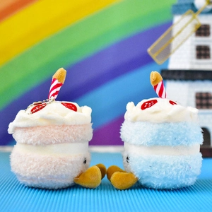 Detailed view of two cake-shaped plush toy pendants in pink and blue with candles.