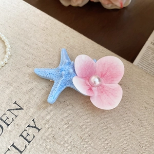 Close-up of starfish and floral hair clip with pearl accent on beige canvas background