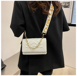 White chevron quilted flap bag with jacquard strap worn over a black blazer