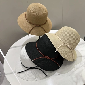 Détail de chapeaux en paille en quatre couleurs avec nœuds en cuir sur une table