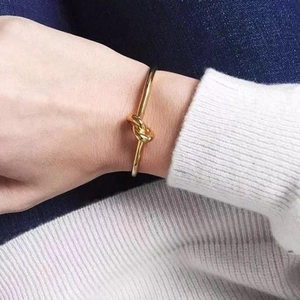 Close-up of a gold knot cuff bracelet worn on a wrist against a casual outfit