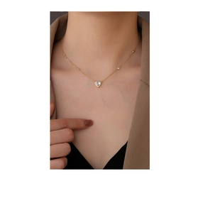 Close-up of heart-shaped gold necklace with zircon stones worn on a model with blazer