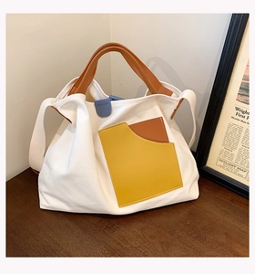 Detail of a white canvas tote bag with brown contrast pocket on a wooden surface