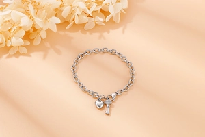 Detail shot of a silver steel chain bracelet featuring heart and key charms on orange