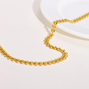Close-up of golden wheat link necklace on white background with minimalist porcelain plate