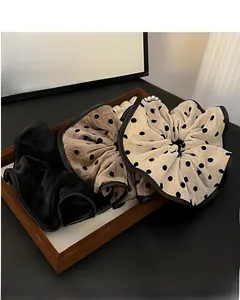 Three oversized polka dot scrunchies in black, brown, and beige on a wooden tray