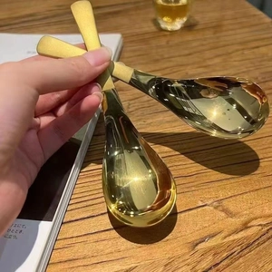 Detail of hand holding two polished gold stainless steel dessert spoons over a wooden table