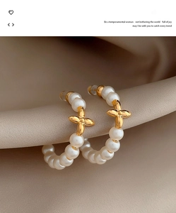 Macro view of C-shaped pearl earrings with golden floral center on beige fabric
