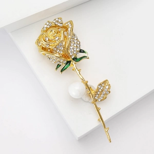 Elegant gold rose brooch with sparkling rhinestones and white pearl on white pedestal