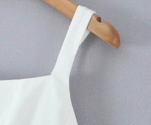 Detailed view of wide shoulder straps on a white cotton dress with natural texture