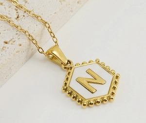 Macro view of gold plated hexagonal pendant with white shell and letter N detail
