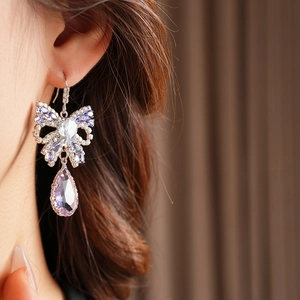 Close-up of elegant bow earrings with purple zircon teardrop pendant on model