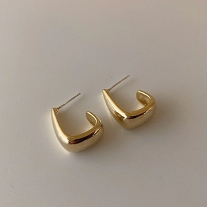 Dettaglio ravvicinato di orecchini geometrici minimalisti in oro lucido a forma di U