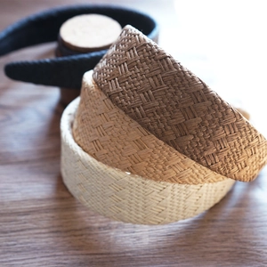 Detail of three stacked straw woven headbands in beige, light brown, and dark brown colors