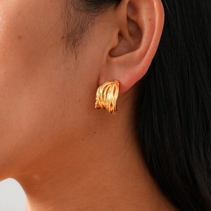 Close-up of golden interlocking multi-loop spiral C-shaped stud earrings worn by a model
