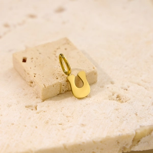 Detail of a polished gold horseshoe pendant on a textured stone surface with modern style