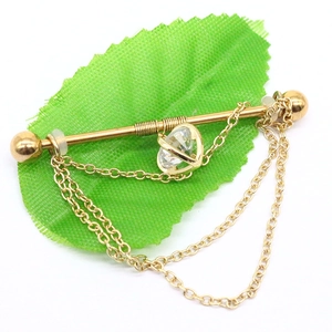 Golden industrial ear piercing with clear zircon stone and double chains on green leaf