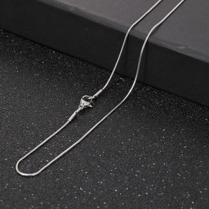 Macro view of a silver snake chain necklace with lobster clasp on a black textured box
