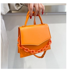 Detail of vibrant orange square handbag with chunky plastic chain and smooth leather texture