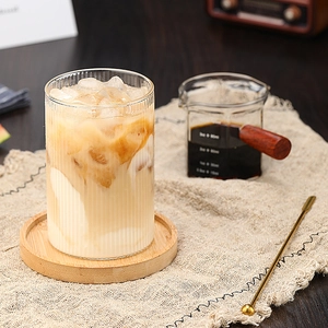 Vaso de vidrio borosilicato con relieve vertical y café helado sobre posavasos de madera