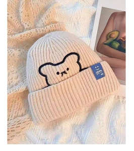 Close-up of beige knitted beanie featuring brown bear embroidery and a blue textile label