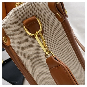 Macro detail of golden metal clasp connecting brown leather strap to beige canvas tote bag