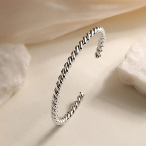 Modern twisted silver bangle with a sleek mirror finish and minimalist C-shaped design