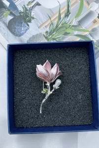 Detail of pink magnolia brooch with pearls on dark velvet padding inside a gift box
