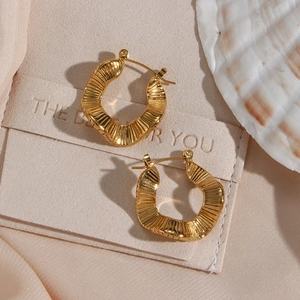 Irregular textured gold earrings in a wave-shaped design displayed on beige velvet