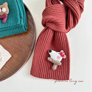 Detailed close-up of chunky knit scarves in terracotta and dark green with cute 3D animal pins