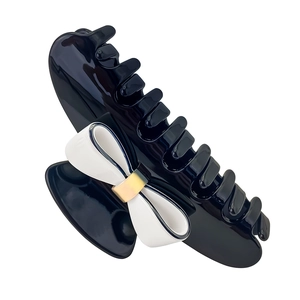 Close-up of black resin hair claw clip with white bow accent and gold metal buckle