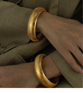 Close-up of dual gold stretch snake texture bangles worn with a green blazer outfit