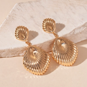 Close-up of golden shell earrings with detailed texture on a warm aesthetic background