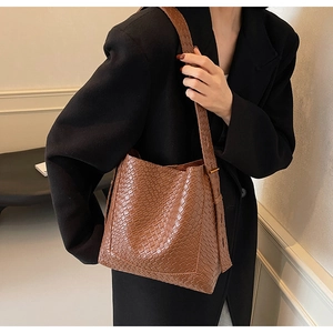 Detailed close-up of brown crocodile pattern bucket bag on model with wide shoulder strap