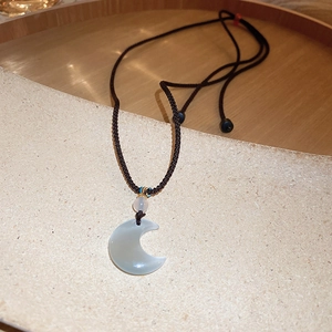 Detail of a crescent moon pendant in translucent grey-white stone with woven brown cord