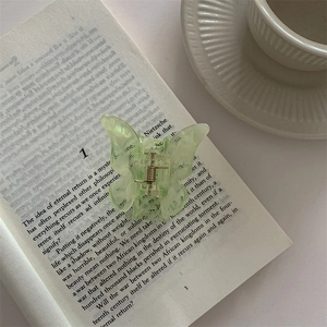 Detail view of a pale green translucent butterfly hair claw clip resting on an open book